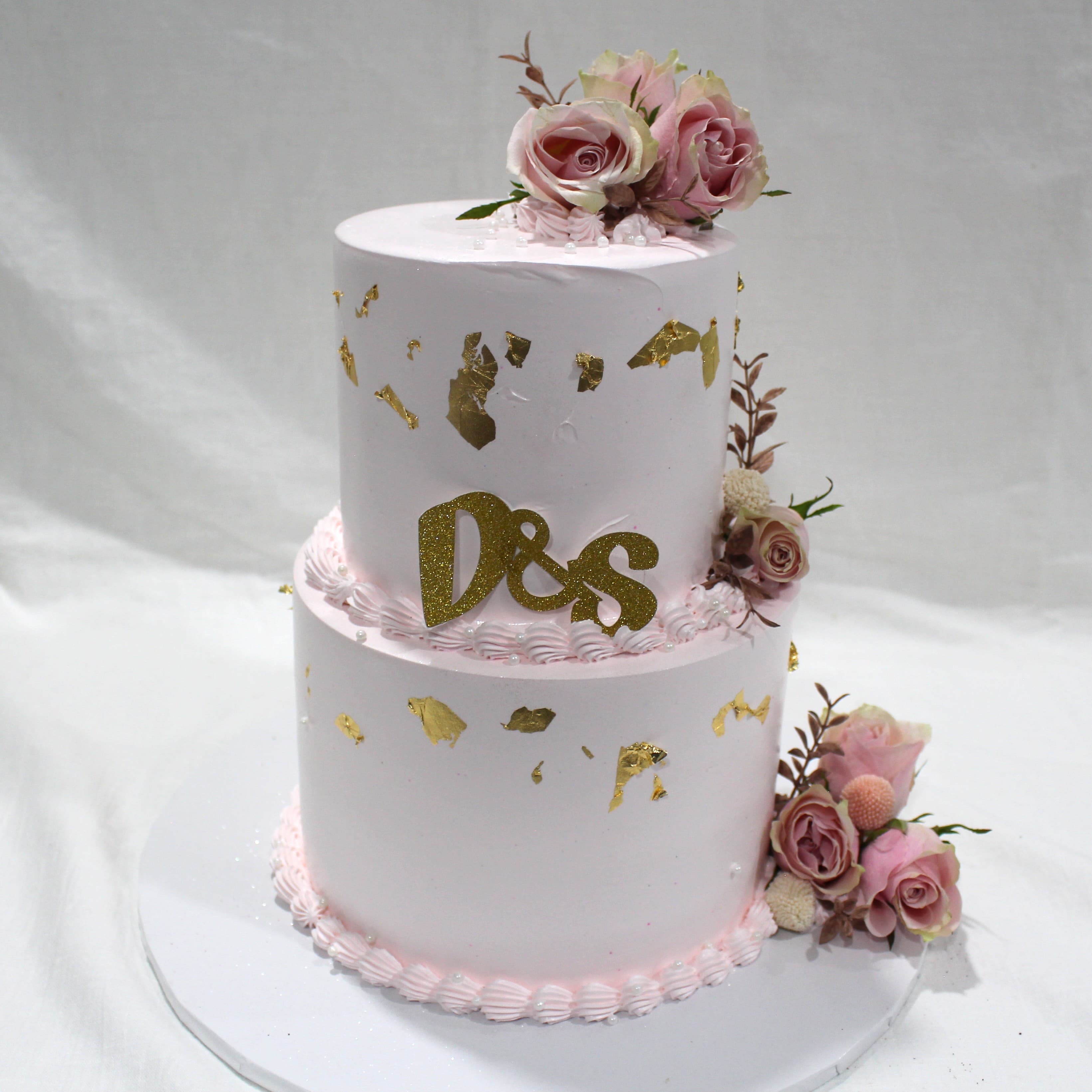 Two-tier blush wedding cake finished with gold leaf and a fresh pink rose topper